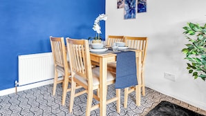 Un coin repas avec un mur bleu, des chaises en bois, une table dressée avec des assiettes, des bols et des verres, et une horloge au mur.