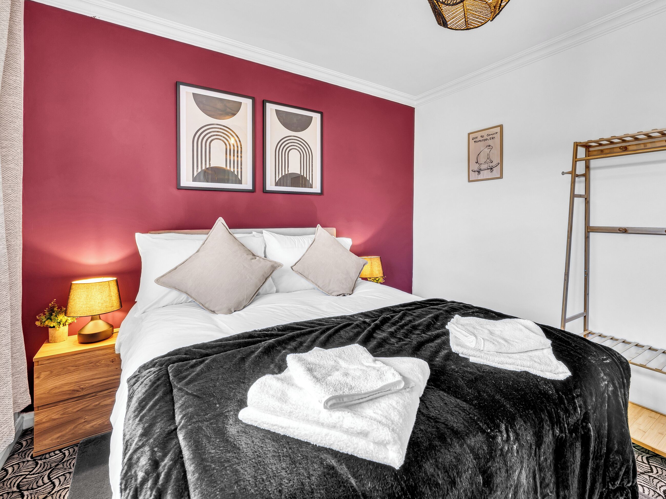 A hotel room with a bed, two bedside lamps, a wooden nightstand, a red wall, and artwork.