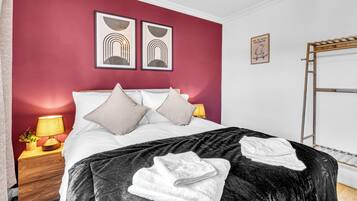 A hotel room with a bed, two bedside lamps, a wooden nightstand, a red wall, and artwork.