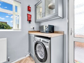 A compact laundry room with a washing machine, a microwave, and a fire blanket.