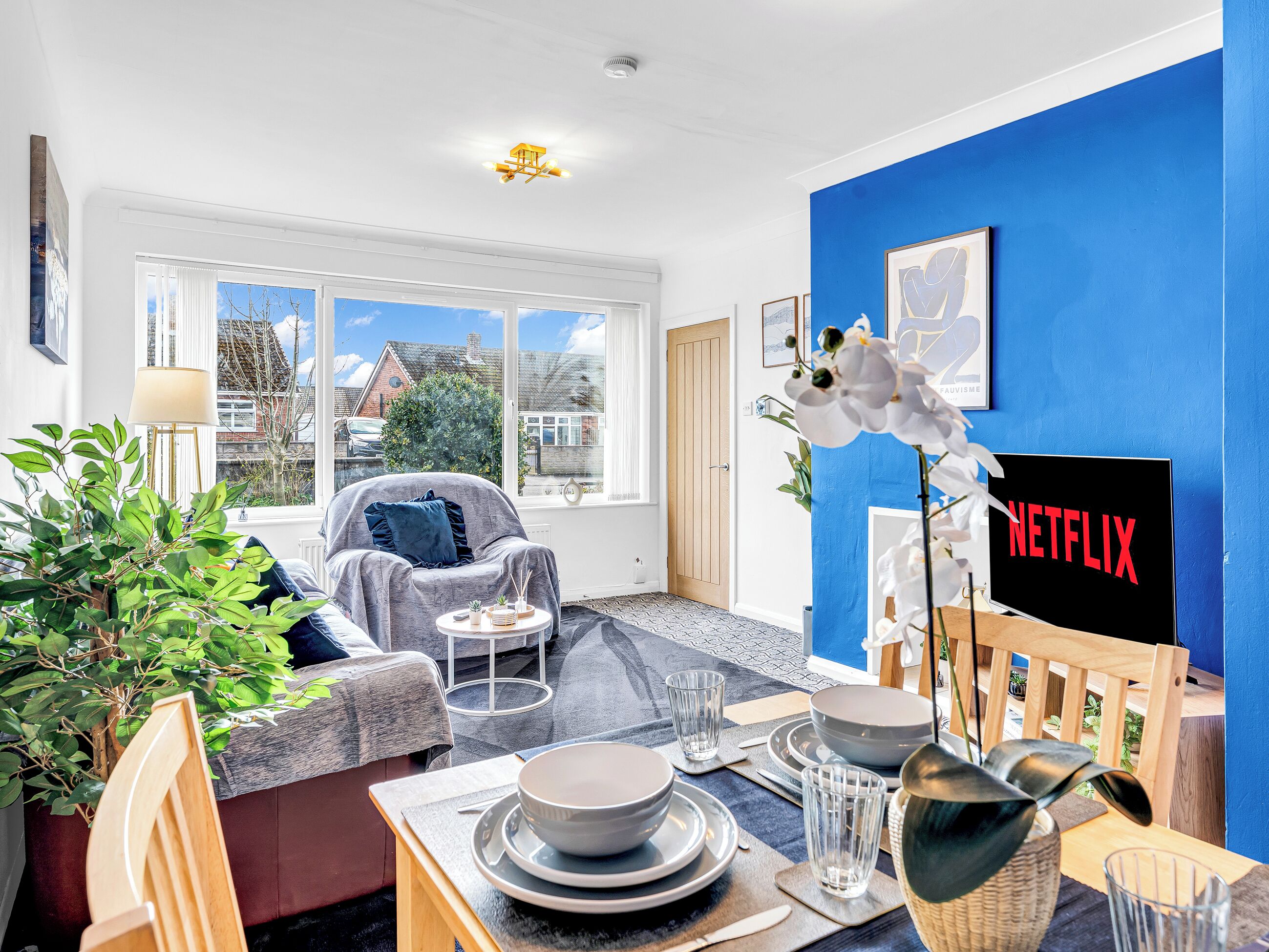 A modern living room with a blue accent wall, a fireplace, and a dining area set with plates and glasses.