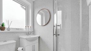 A bathroom with a toilet, sink, mirror, and shower. - 3 bedroom accommodation in Leek (Leek)