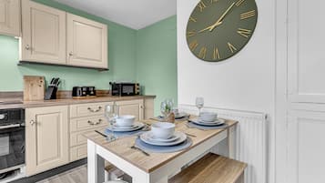 A kitchen with a dining table set for two, a microwave, and a clock on the wall.