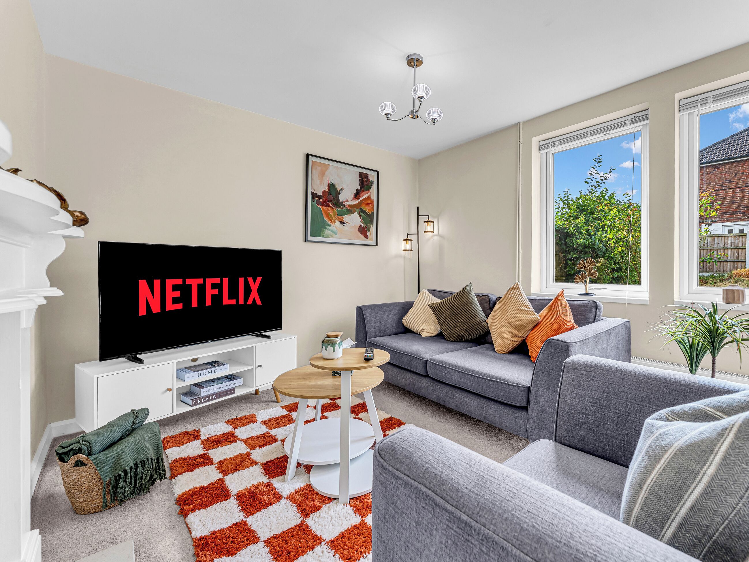 Uma sala de estar com uma televisão exibindo 'NETFLIX', um sofá, uma mesa de centro e vista para o verde lá fora.