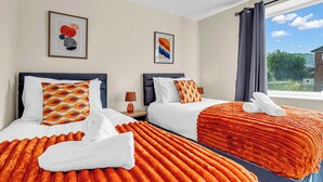 A hotel room with two beds, each with an orange blanket and white pillows, a bedside table with a lamp, and a window with a view of greenery. - 3 bedroom accommodation in Leek (Leek)