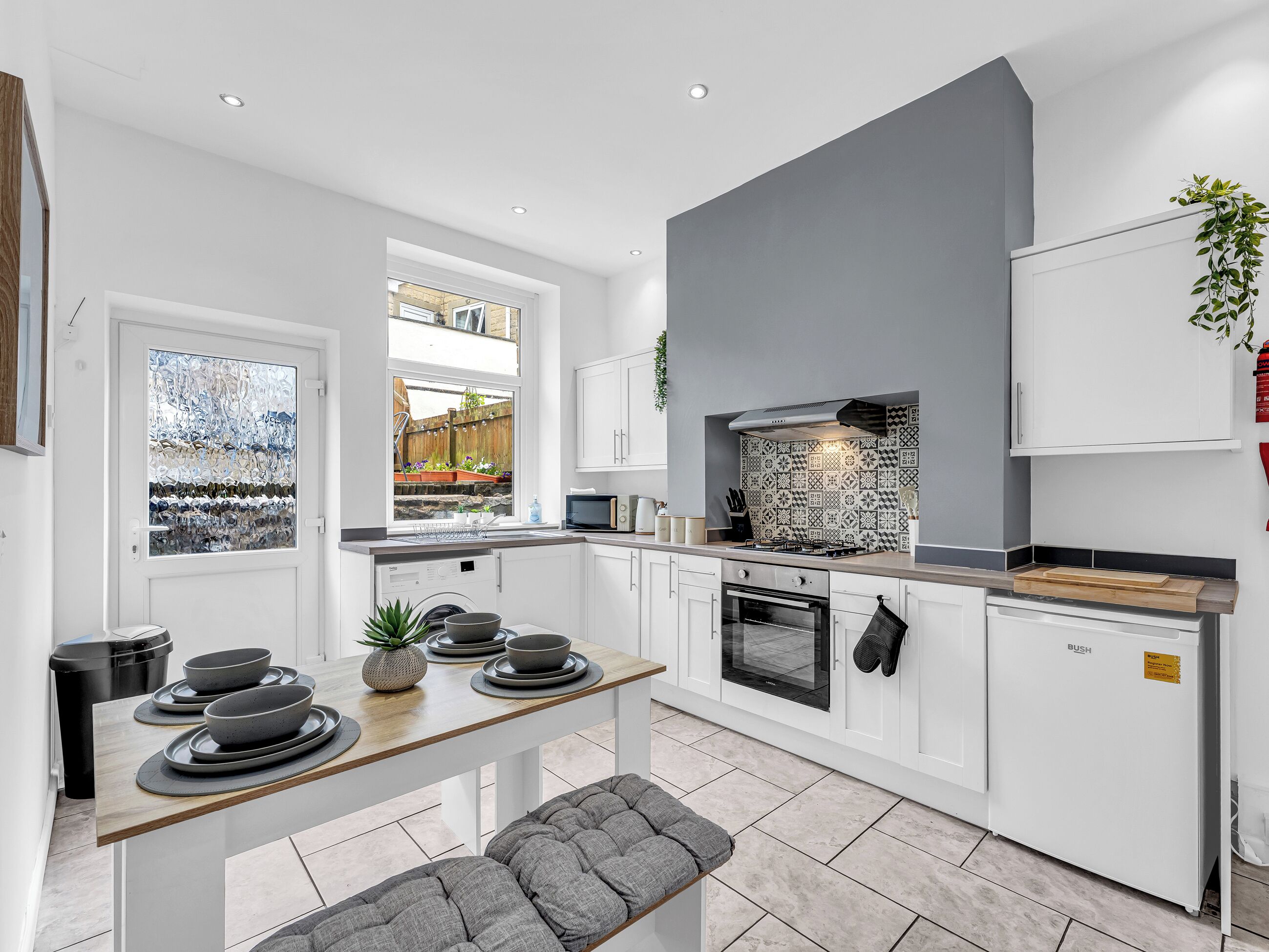 A modern kitchen with white cabinetry, a grey accent wall, a built-in oven, and a window overlooking a garden.