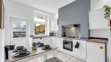 A modern kitchen with white cabinetry, a grey accent wall, a built-in oven, and a window overlooking a garden.