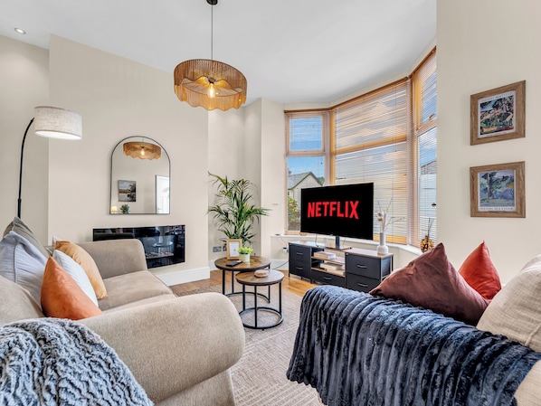 Una sala de estar moderna con una televisión mostrando 'NETFLIX', un sofá, una mesa de centro y un ventanal con persianas.