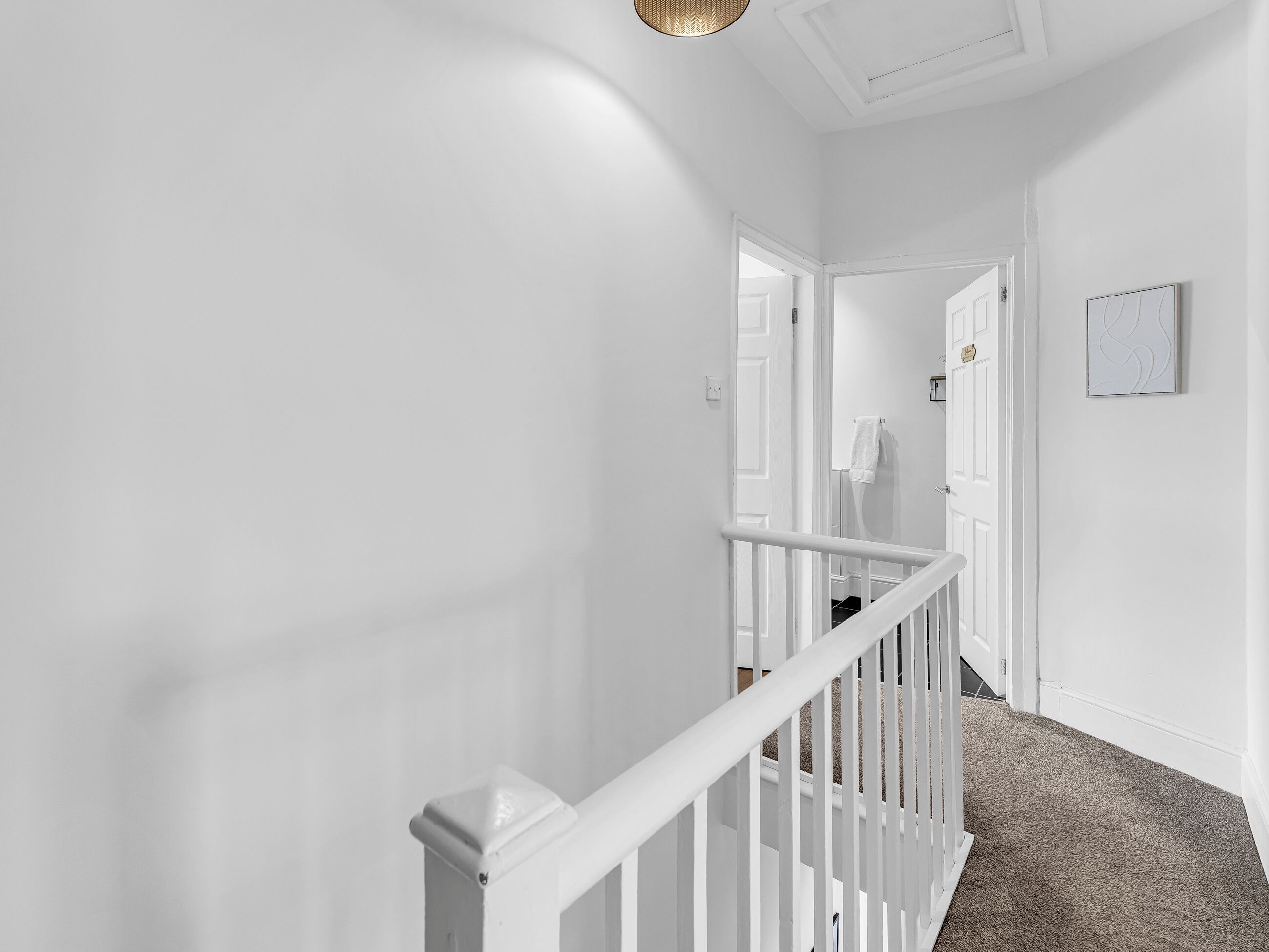 A hallway with white walls, a white railing, and a carpeted floor.