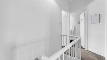 A hallway with white walls, a white railing, and a carpeted floor.