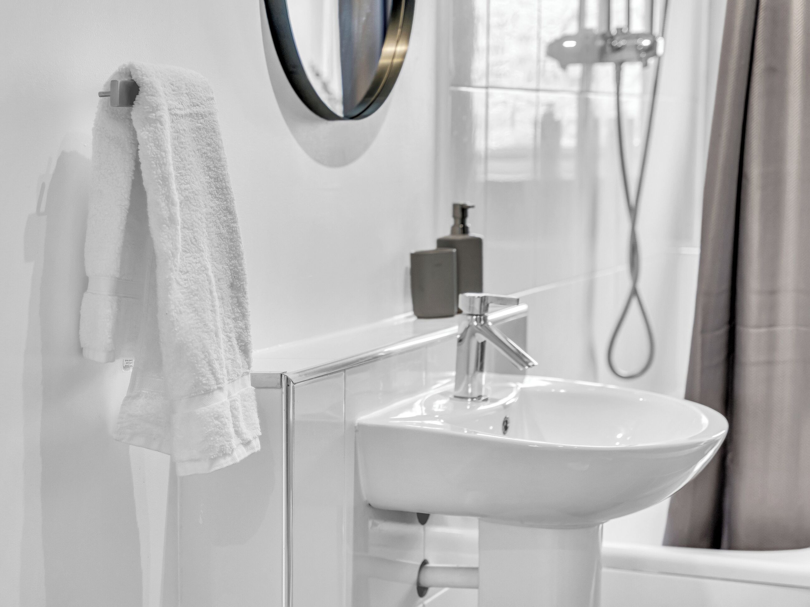 A bathroom with a white sink, a mirror, and a towel hanging on the wall.