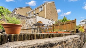 A patio with a table and chairs, a potted plant, and a stone wall. - A terraced cottage on Leek Road, positioned for Buxton and the Peak District. (Buxton)