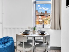 A dining area with a table set for four, chairs, a blue bean bag, and a view of a residential street through a window. - 3 bedroom accommodation in Stoke-on-Trent (Stoke-on-Trent)