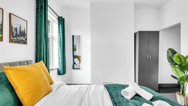 Hotellihuone, jossa on sänky, vaatekaappi, peili ja ikkuna, jossa on verhot.