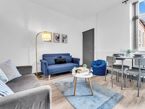 A modern living room with a blue sofa, a grey armchair, a coffee table, and a dining area with a table and chairs. - 3 bedroom accommodation in Stoke-on-Trent (Stoke-on-Trent)