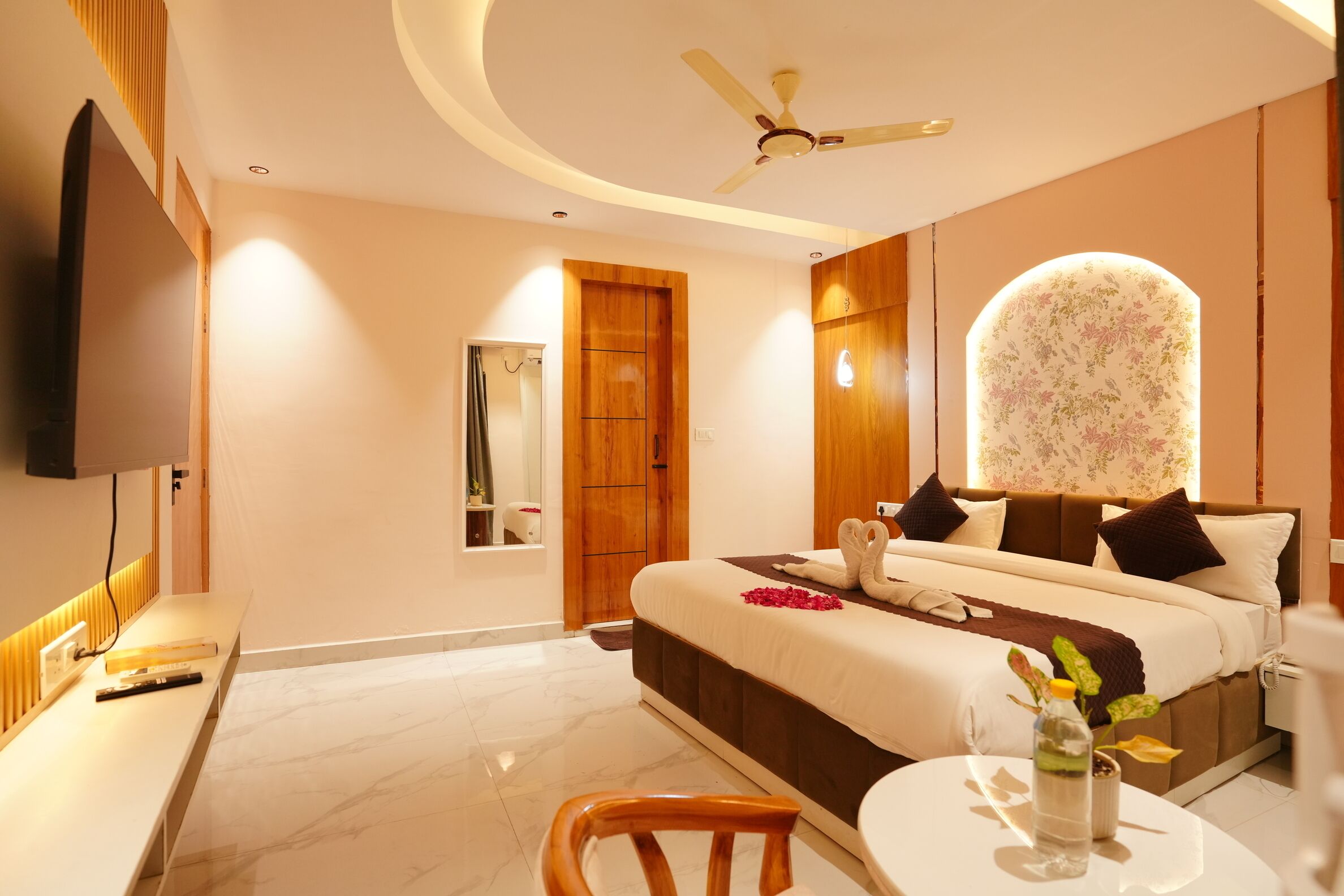 Habitación de hotel moderna con cama, escritorio, silla, televisión y ventilador de techo.