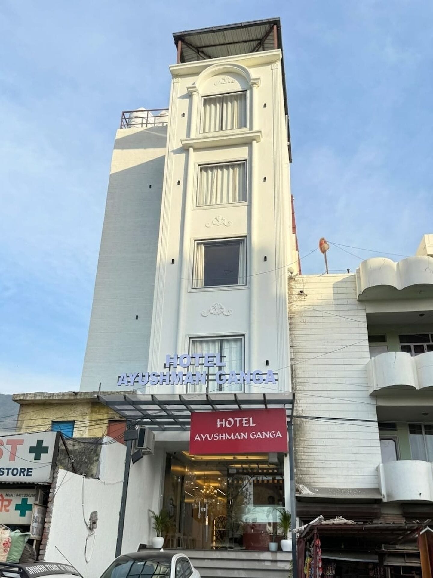 Un hotel llamado 'Hotel Ayushman Ganga' con una fachada moderna, una entrada visible y un letrero.