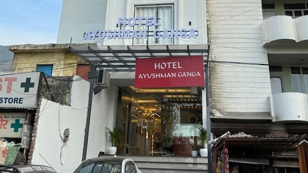 Ein Hotel namens 'Hotel Ayushman Ganga' mit moderner Fassade, einem gut sichtbaren Eingang und einem Schild.