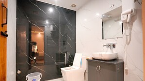 Ein modernes Badezimmer mit schwarzem Marmor an der Wand, einem weißen Waschbecken, einem Spiegel und einem an der Wand befestigten Fön.