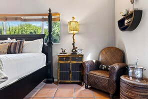 Une chambre à coucher avec un lit, une table de chevet avec une lampe, une chaise et une petite table sur laquelle se trouvent un verre et une bouteille de vin.