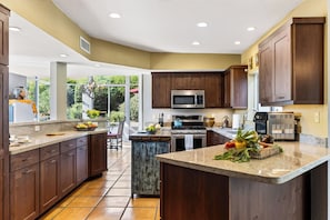 A modern kitchen with dark wood cabinets, stainless steel appliances, and a large island with fresh produce. - Hot Tub + Covered Dining + Grill | Red Rock Views | Sage & Sandstone (Sedona)