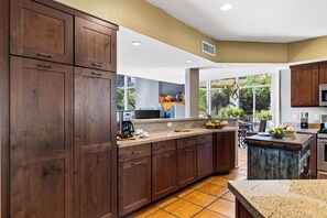 A kitchen with dark wooden cabinets, a granite countertop, and a view of the outdoors through large windows. - Hot Tub + Covered Dining + Grill | Red Rock Views | Sage & Sandstone (Sedona)