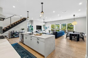 Eine moderne Küche mit Kochinsel, ein Essbereich mit Tisch und Stühlen, ein blaues Sofa und eine Treppe mit Holzstufen.