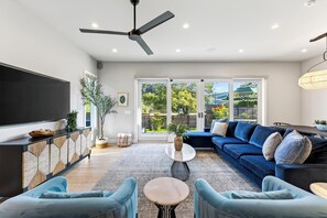 Ein modernes Wohnzimmer mit Flachbildfernseher, Deckenventilator, einer Sofagarnitur und einem Essbereich mit Tisch und Stühlen.