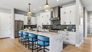 A modern kitchen with a central island, bar stools, stainless steel appliances, and pendant lighting. - Private Pool + Hot Tub + Game Room + Gym | Hill Country Views | River Bend (Austin)