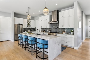 A modern kitchen with a central island, bar stools, stainless steel appliances, and pendant lighting. - Private Pool + Hot Tub + Game Room + Gym | Hill Country Views | River Bend (Austin)
