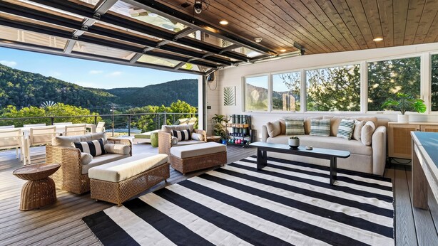 A spacious outdoor living area with a wooden deck, outdoor furniture, and a view of the mountains. - Private Pool + Hot Tub + Game Room + Gym | Hill Country Views | River Bend (Austin)