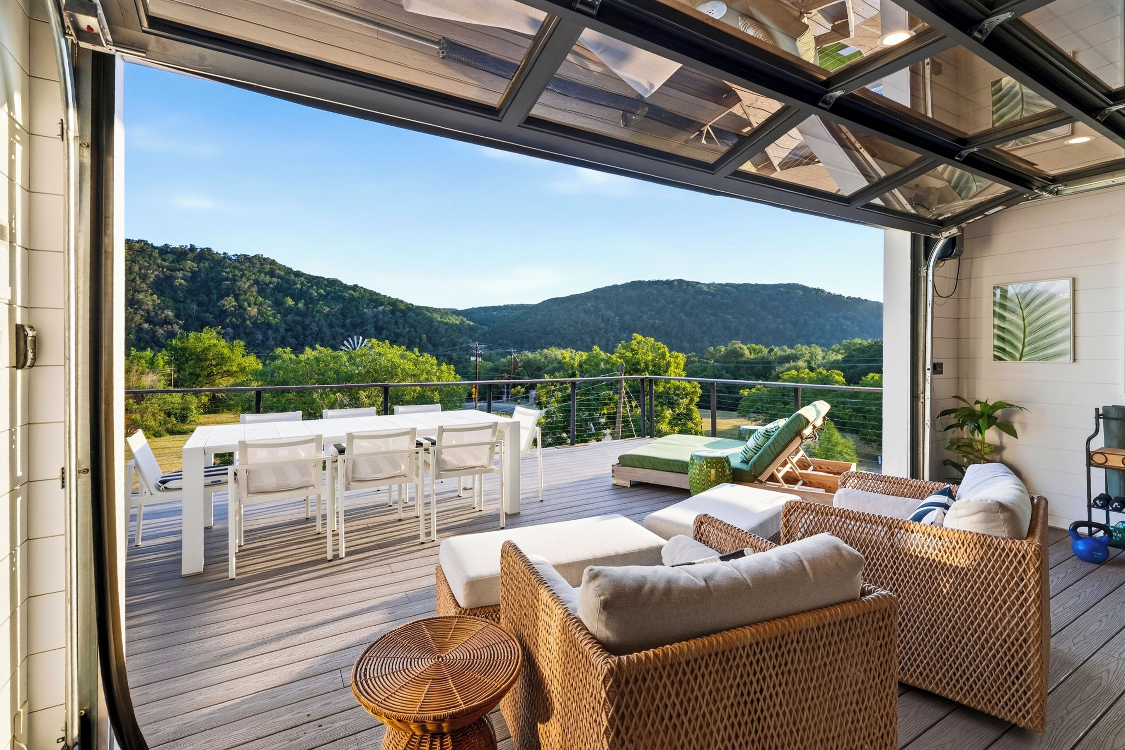 An open deck with outdoor furniture, a view of green hills, and a clear sky.