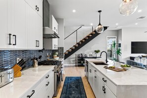 A modern kitchen with a central island, a built-in stove, and a staircase leading to a living area. - Private Pool + Hot Tub + Game Room + Gym | Hill Country Views | River Bend (Austin)
