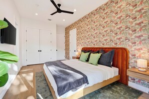 A bedroom with a bed, a ceiling fan, a nightstand, a lamp, and a wall with a floral pattern. - Private Pool + Hot Tub + Game Room + Gym | Hill Country Views | River Bend (Austin)