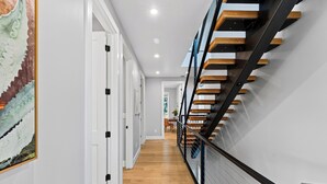 A hallway with a wooden floor, white walls, and a staircase with wooden steps and black railings. - Private Pool + Hot Tub + Game Room + Gym | Hill Country Views | River Bend (Austin)