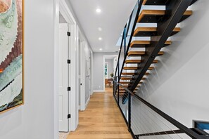 A hallway with a wooden floor, white walls, and a staircase with wooden steps and black railings. - Private Pool + Hot Tub + Game Room + Gym | Hill Country Views | River Bend (Austin)