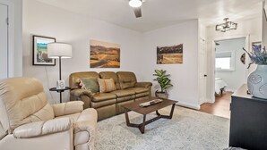 A living room with a sofa, armchair, coffee table, and a ceiling fan. There are framed pictures on the wall and a potted plant. - 3 BRs + Firepit + BBQ + Cornhole | Two Decks | Paso + Hideaway on Oak (Paso Robles)
