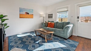 A living room with a blue patterned rug, a light blue sofa, a wooden coffee table, a painting of a field, and a ceiling fan. - 3 BRs + Firepit + BBQ + Cornhole | Two Decks | Paso + Hideaway on Oak (Paso Robles)
