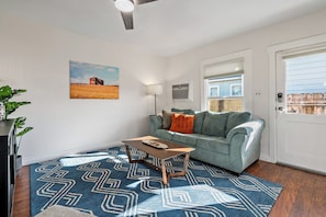 A living room with a blue patterned rug, a light blue sofa, a wooden coffee table, a painting of a field, and a ceiling fan. - 3 BRs + Firepit + BBQ + Cornhole | Two Decks | Paso + Hideaway on Oak (Paso Robles)