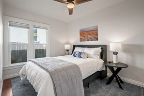 Une chambre à coucher avec un lit, deux lampes de chevet, une table de nuit, un tableau au mur et une fenêtre donnant sur un paysage.