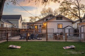 Ein Wohnhausgarten mit Holzterrasse, Gartenmöbeln und einer Lichterkette.