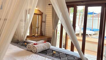 A bed with a canopy, a wooden bench, a mirror, and a view of an outdoor pool area.