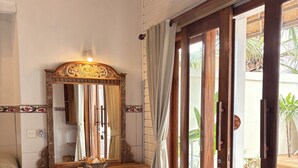 A room with a wooden vanity, a large mirror, a door leading outside, and a tiled floor.