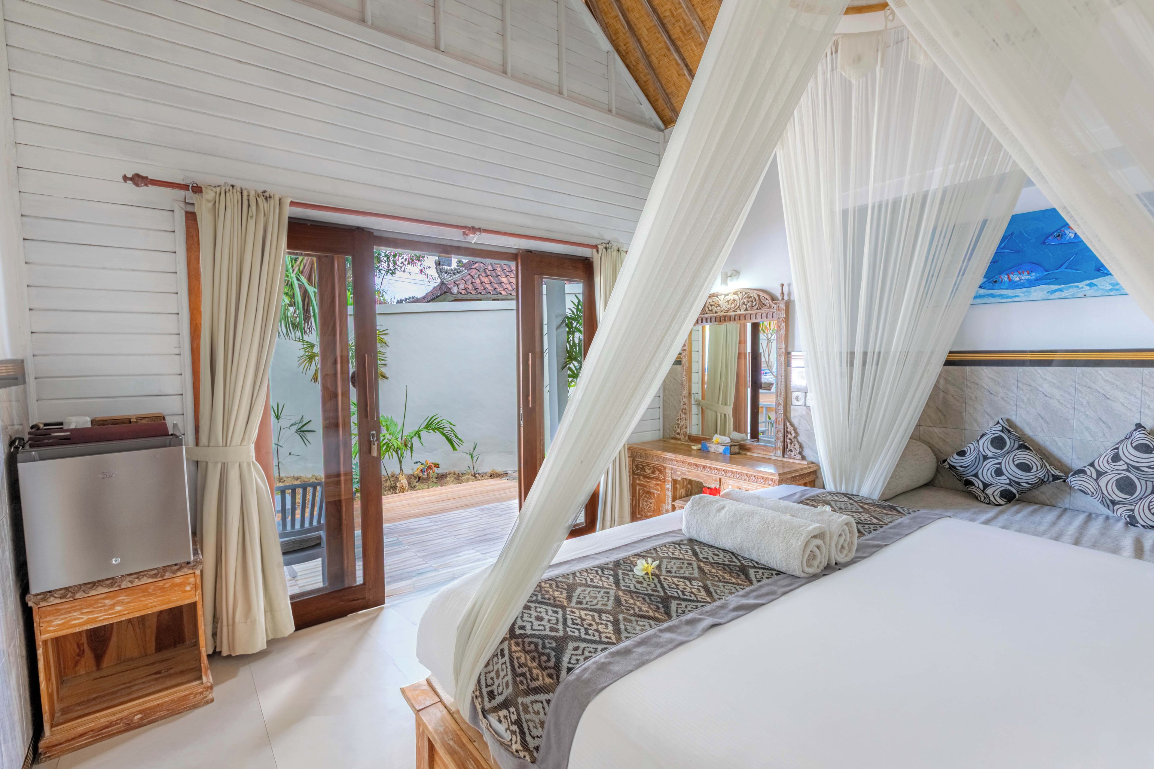 A bedroom with a bed, a nightstand, a mirror, and a view of the outdoors.