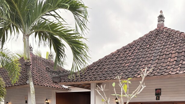 A poolside area with a tiled pool, wooden deck, and a building with a tiled roof and white walls.
