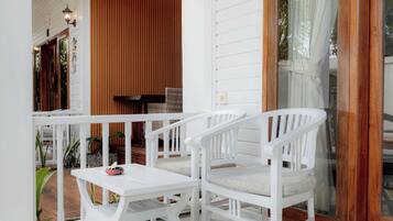 Uma área de estar ao ar livre com cadeiras e mesa, parede de madeira e porta de vidro.