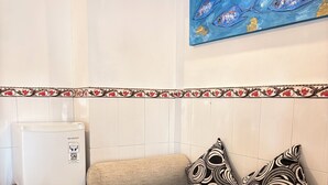 A room with a sofa, patterned pillows, a painting of fish, a white refrigerator, and a decorative tile border.