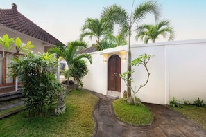 A traditional house with a tiled roof, a wooden door, and a small garden with palm trees and a pathway. - Blue Lagoon Private Villa (Bali)