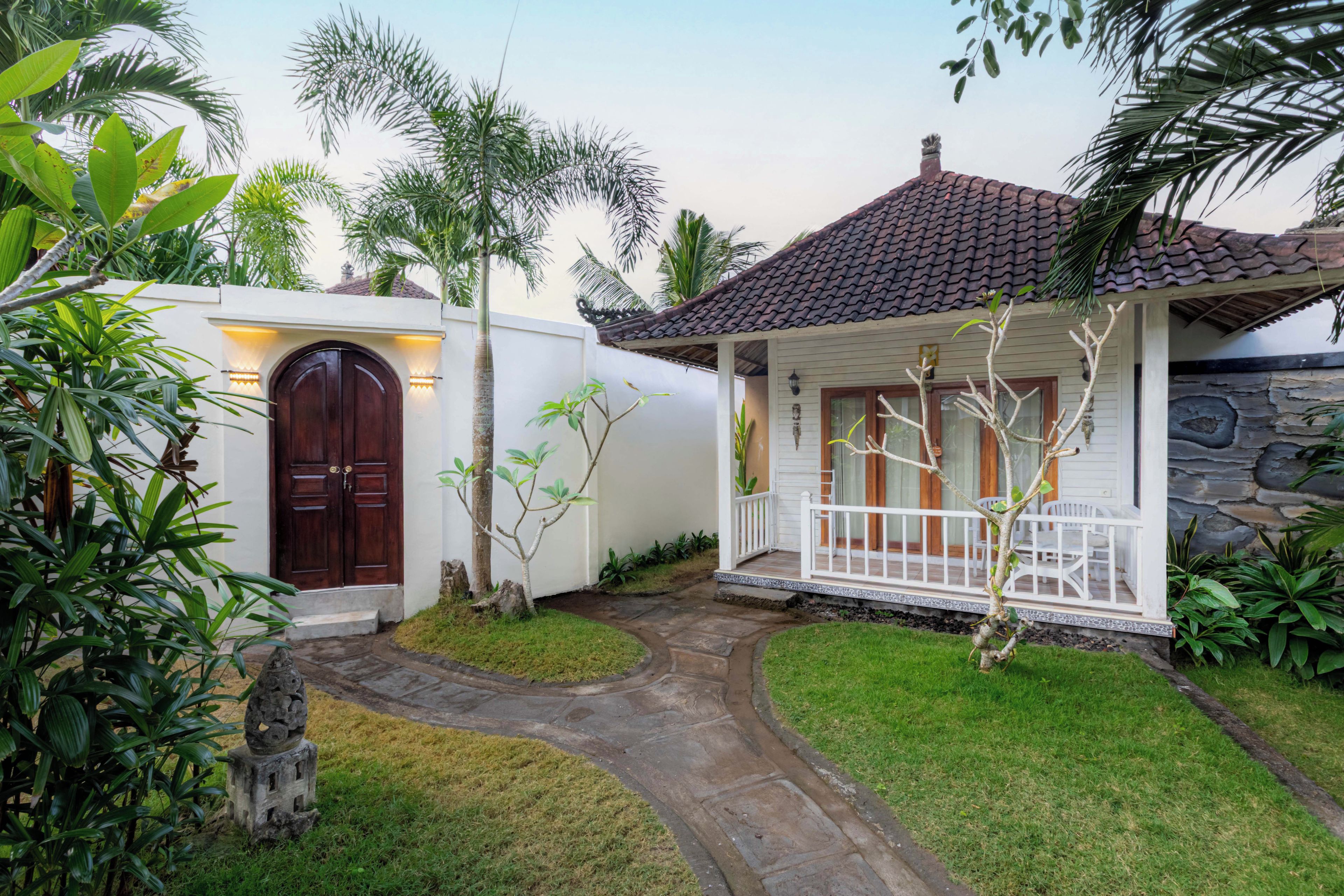 A two-story house with a tiled roof, a stone wall, and a white porch with a railing.