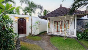 A two-story house with a tiled roof, a stone wall, and a white porch with a railing.